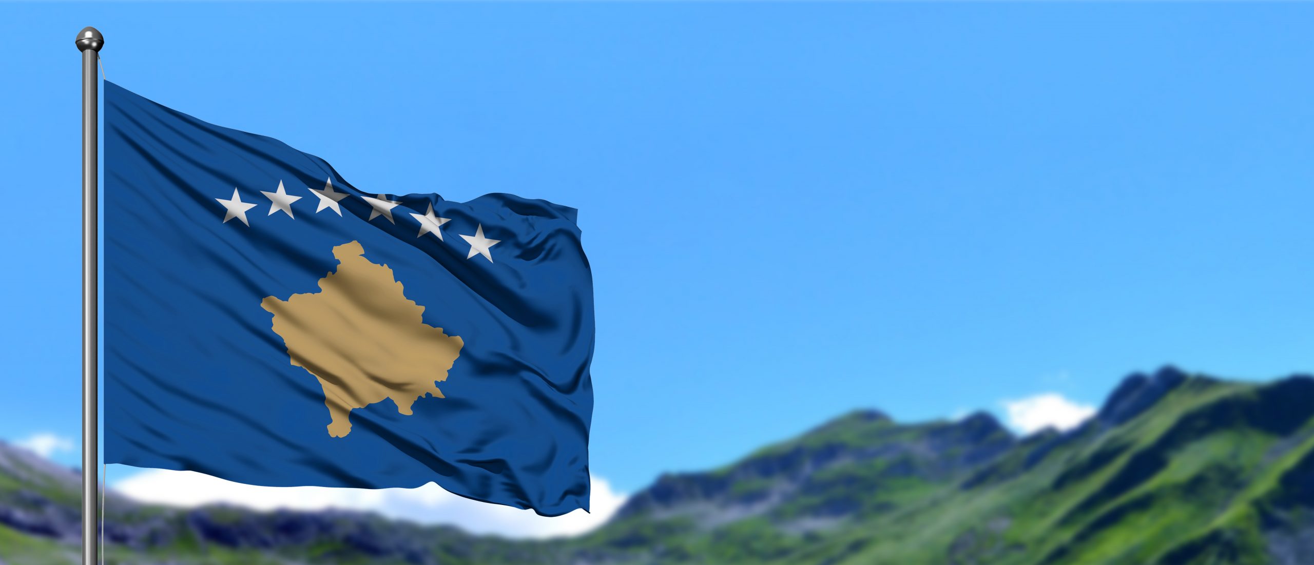 Kosovo flag waving in the blue sky with green fields at mountain peak background. Nature theme.